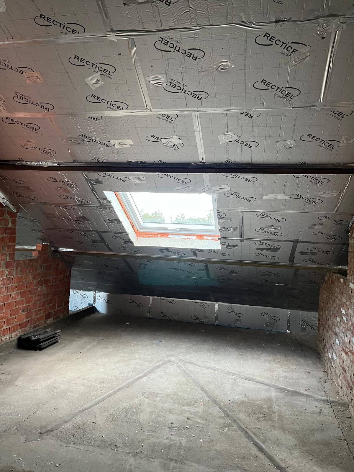 Geïsoleerde zolderruimte met een Velux-dakraam en zicht op bakstenen muur
