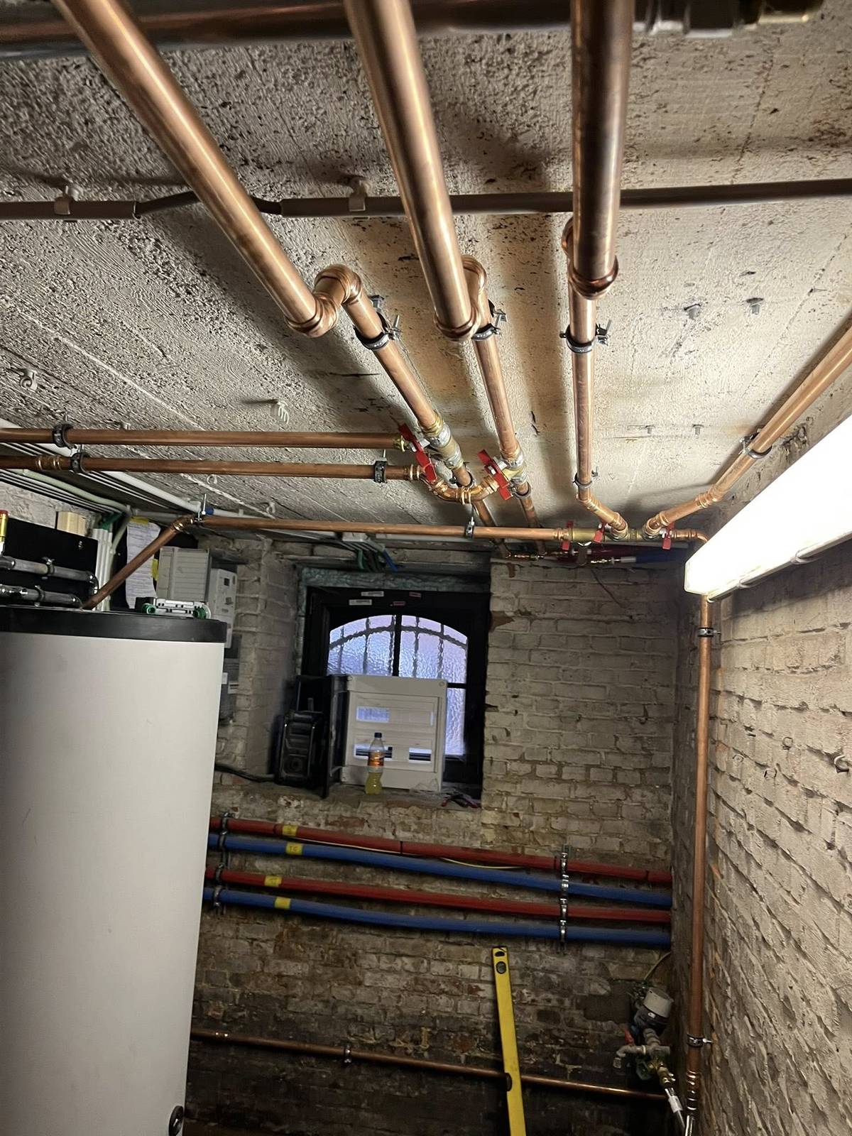 Zicht op koperen leidingen en een warmwaterboiler in een kelderruimte