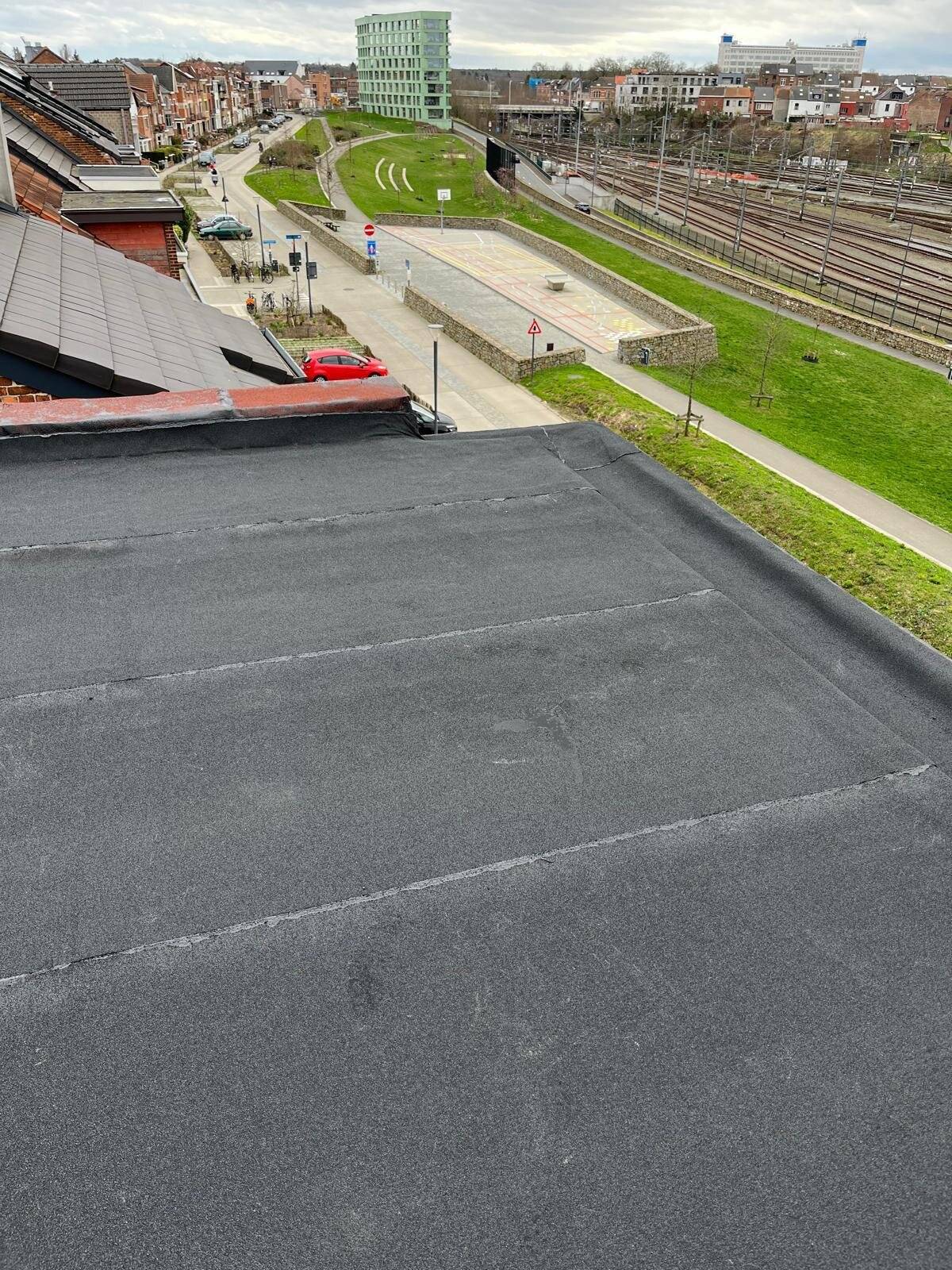 Uitzicht vanaf een plat dak over een stedelijke omgeving met spoorlijn en gebouwen.