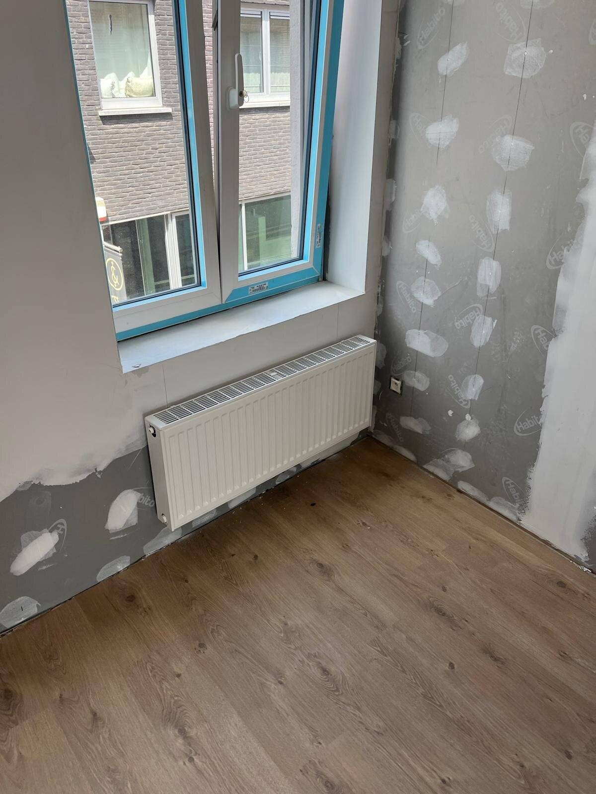 Witte radiator onder een raam in een ruimte die klaargemaakt wordt voor schilderwerken.