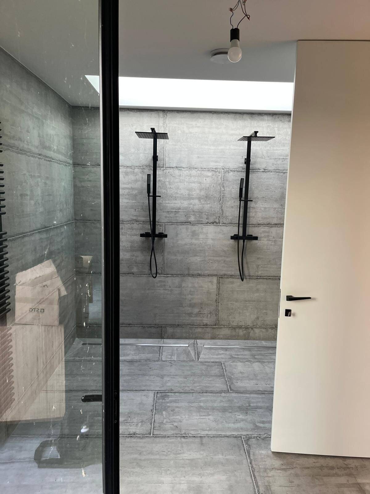 Moderne badkamer met inloopdouche en twee zwarte regendouches tegen een betonnen muur.